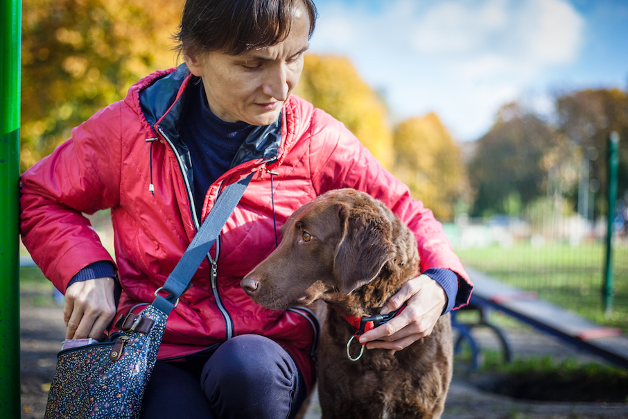 Kobieta w czerwonej kurtce karmi przysmakami swojego psa przewodnika